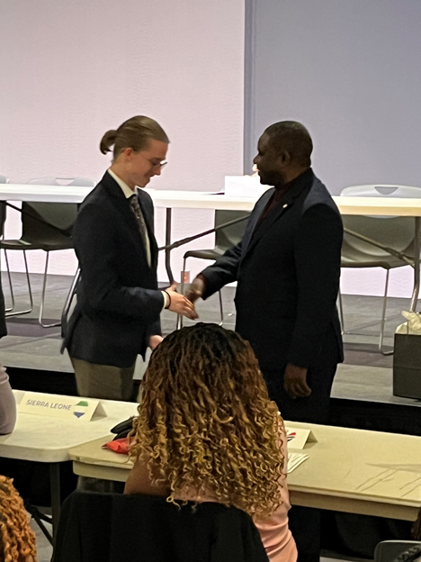 UGA SEMAU Delegation team leader, Phillips receiving the ''SEMAU 2023 Most Outstanding Delegation award from Ambassador Kanyama